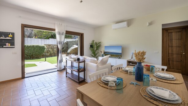 A dining area with a table set for two, a sofa, and a TV in the background. - Apartment 'Flat Arcipelago' with Shared Pool, Wi-Fi and Air Conditioning (Palau)