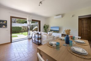 A dining area with a table set for two, a sofa, and a TV in the background.