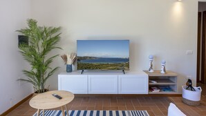 A living room with a flat-screen TV, a potted plant, a small table, a white cabinet, and a wall-mounted air conditioner. - Apartment 'Flat Arcipelago' with Shared Pool, Wi-Fi and Air Conditioning (Palau)
