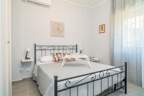 A neatly arranged bedroom with a bed, bedside tables, a wall-mounted air conditioner, and a window with curtains.