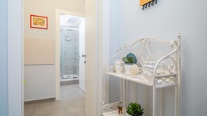 A hallway with a white metal shelf holding decorative items, a door leading to a shower area, and a wall-mounted coat rack. - Apartment 'Al Nitta 2' with Wi-Fi and Air Conditioning (Catania)