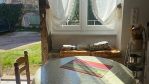 Uma mesa redonda com toalha de bolinhas, uma cadeira de madeira e uma janela com cortinas finas.