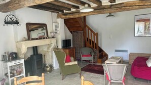 Uma sala de estar rústica com vigas de madeira aparentes, lareira, móveis de vime e uma escada.