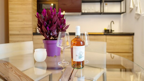 Une cuisine moderne avec des meubles en bois, une plante violette et une bouteille de vin posée sur une table en verre.