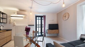 Un salon moderne comprenant un canapé, un téléviseur, une table à manger avec des chaises, ainsi qu’un coin cuisine avec des placards et un plan de travail.