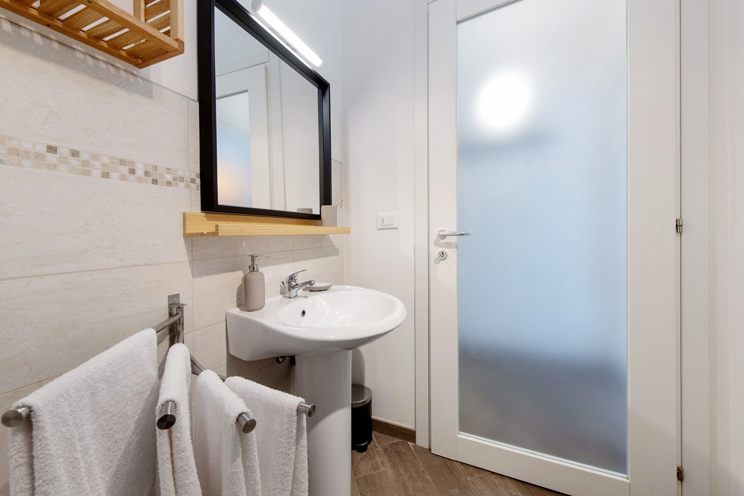 A bathroom with a white sink, a mirror, a towel rack with white towels, and a frosted glass door.