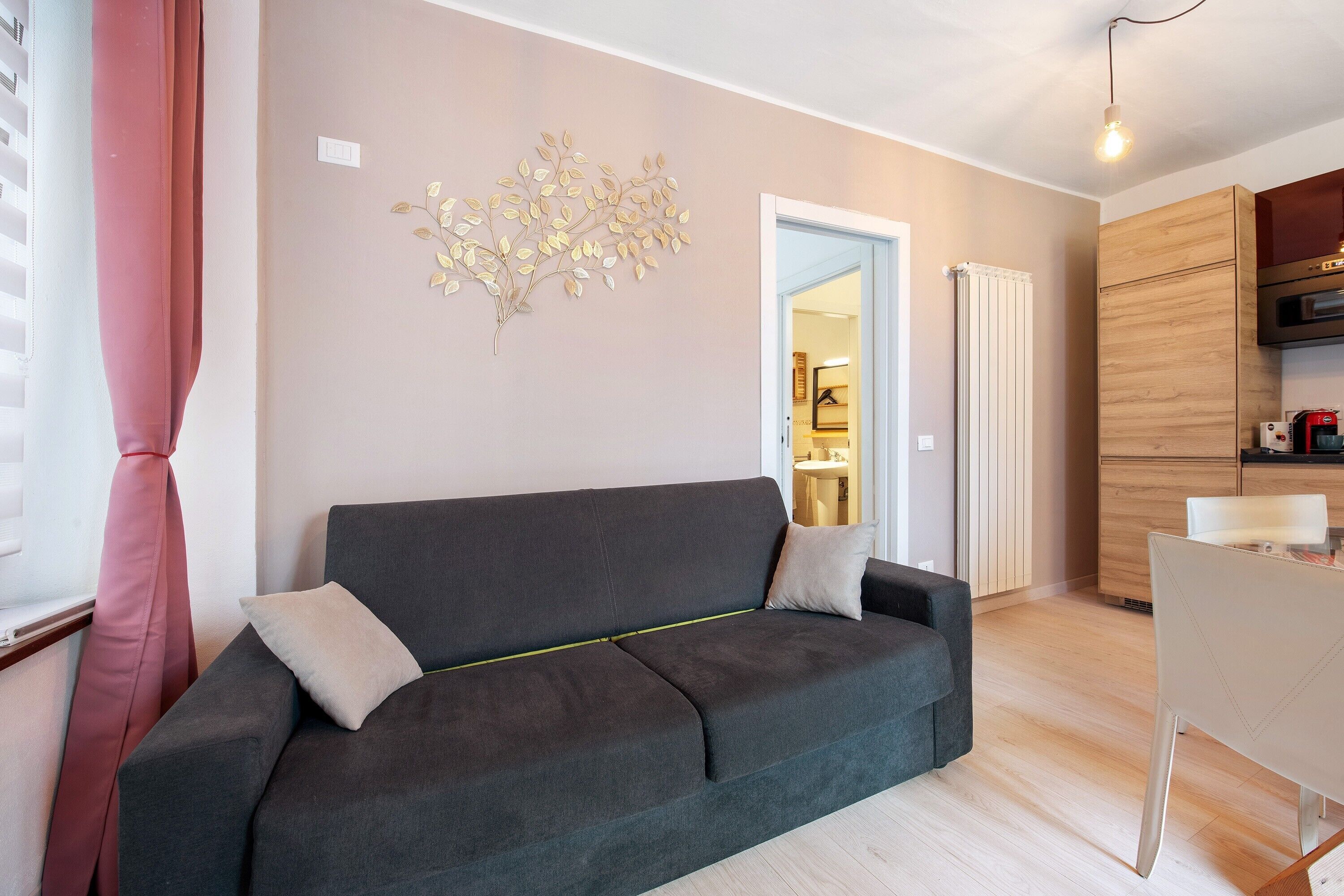 A modern living room with a grey sofa, a decorative wall piece, and a wooden kitchen area.