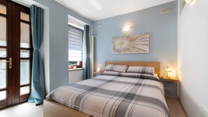 Une chambre à coucher avec un lit, une fenêtre avec des rideaux, une table de chevet avec une lampe et un luminaire fixé au mur.