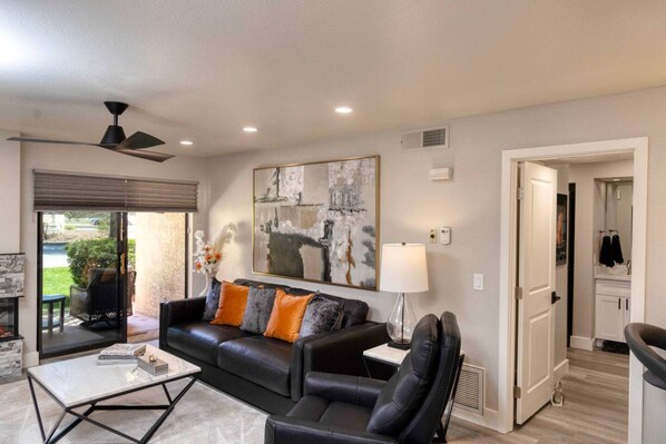 A modern living room with a black leather sofa, a glass coffee table, and a large abstract painting on the wall.