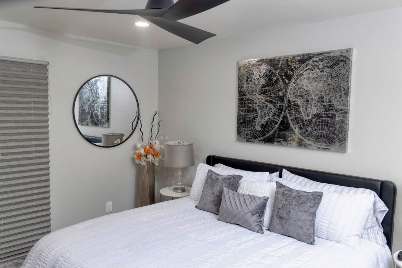 Une chambre à coucher avec un lit, un miroir rond, une lampe et une œuvre d’art représentant une carte du monde accrochée au mur.