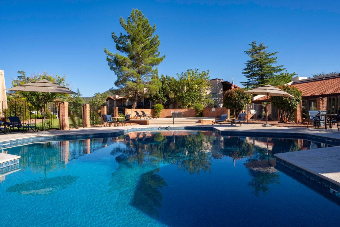 A swimming pool with lounge chairs and umbrellas, surrounded by trees and buildings.