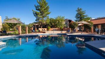 A swimming pool with lounge chairs and umbrellas, surrounded by trees and buildings.