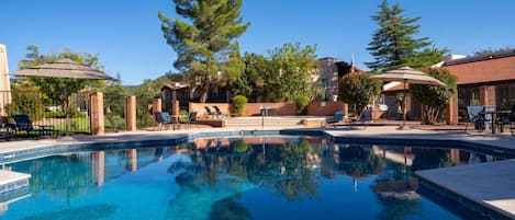 A swimming pool with lounge chairs and umbrellas, surrounded by trees and buildings.