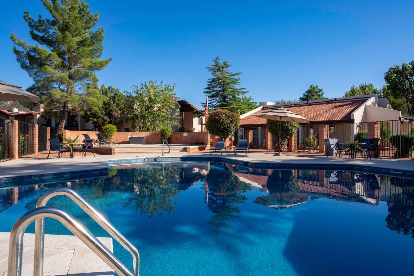 A swimming pool with lounge chairs and umbrellas, surrounded by buildings with red-tiled roofs and brick walls.