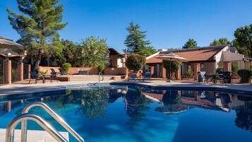 A swimming pool with lounge chairs and umbrellas, surrounded by buildings with red-tiled roofs and brick walls.