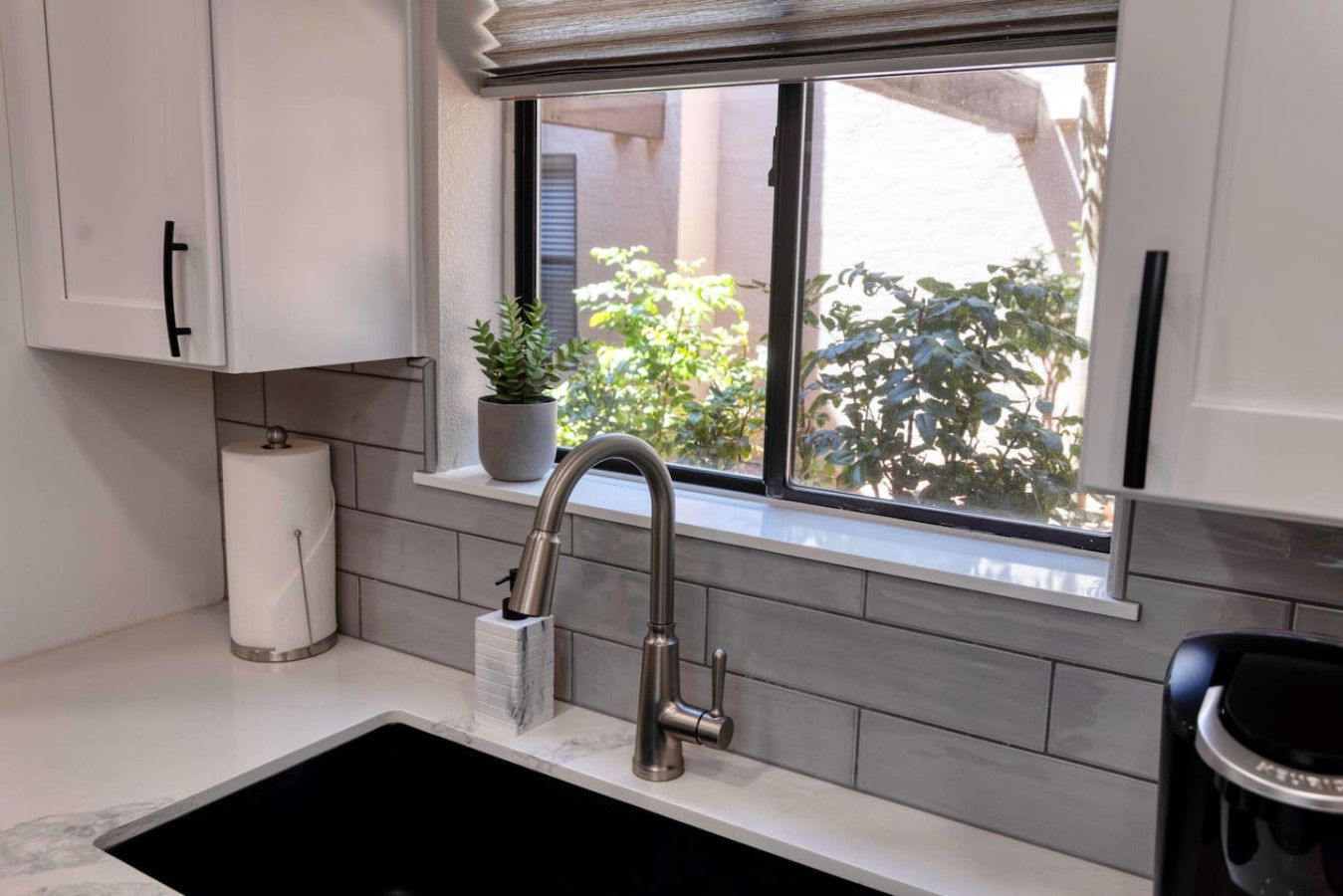 A kitchen with a window, a sink, a potted plant, and a trash can.