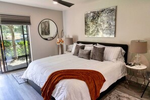 A modern bedroom with a large bed, a round mirror, a globe artwork, and a view of greenery outside. - Sultry Sedona Getaway (Sedona)