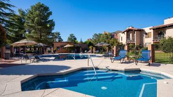 A swimming pool area with lounge chairs and umbrellas, surrounded by buildings and trees.