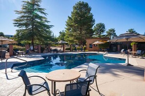 A swimming pool with lounge chairs and umbrellas, surrounded by trees and a brick building. - Sultry Sedona Getaway  (Sedona)