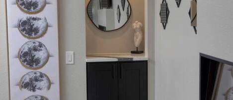 Un couloir orné d’une œuvre d’art encadrée représentant des lunes, d’un miroir rond et de divers éléments décoratifs fixés au mur.