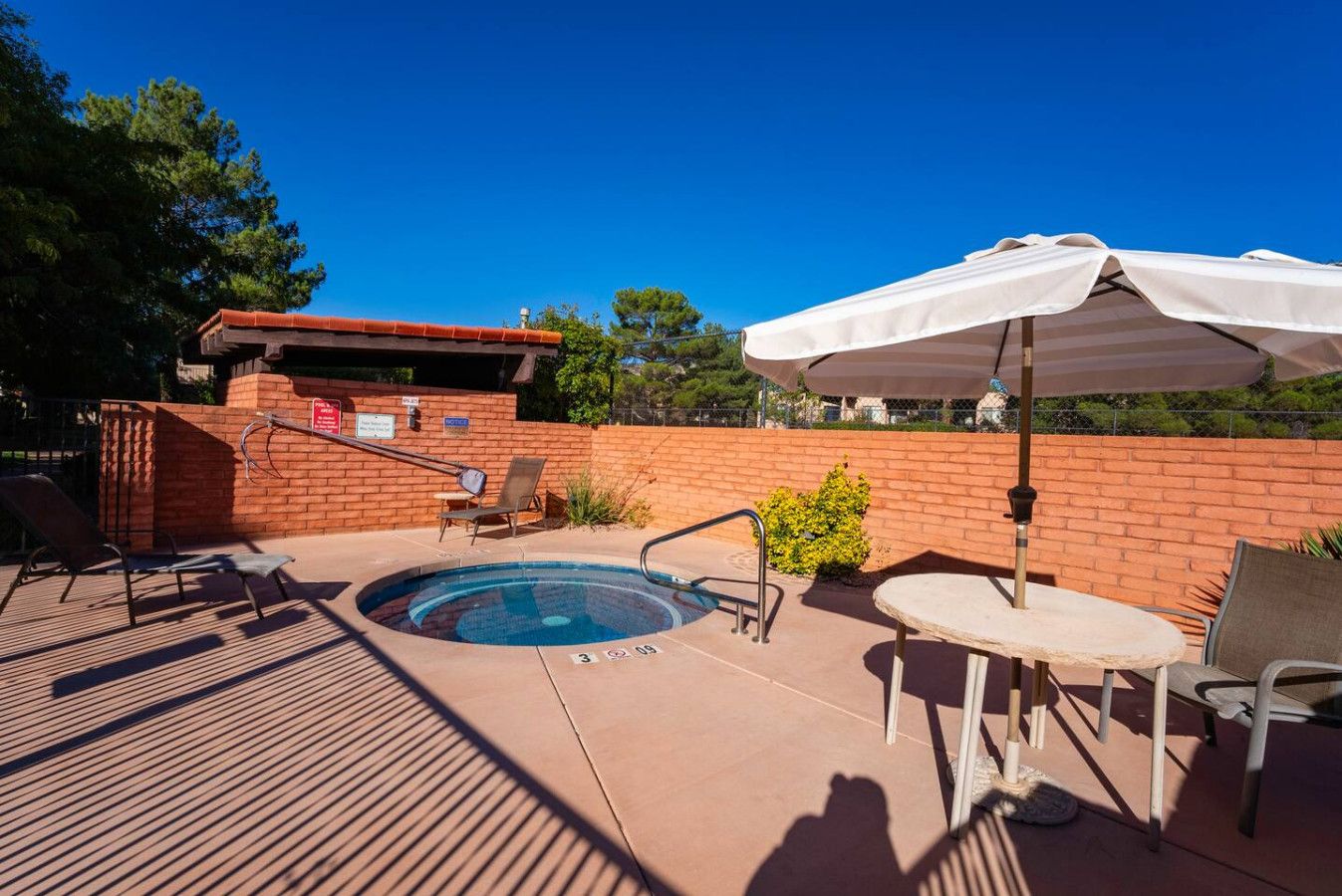 A pool area with a hot tub, lounge chairs, and a table with an umbrella.