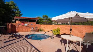 A pool area with a hot tub, lounge chairs, and a table with an umbrella.