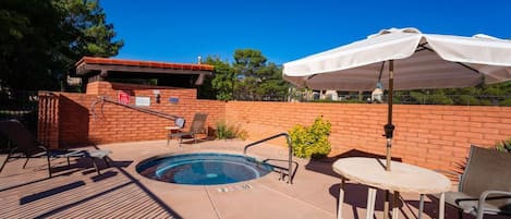 Un área de piscina con jacuzzi, sillones de descanso y una mesa con sombrilla.