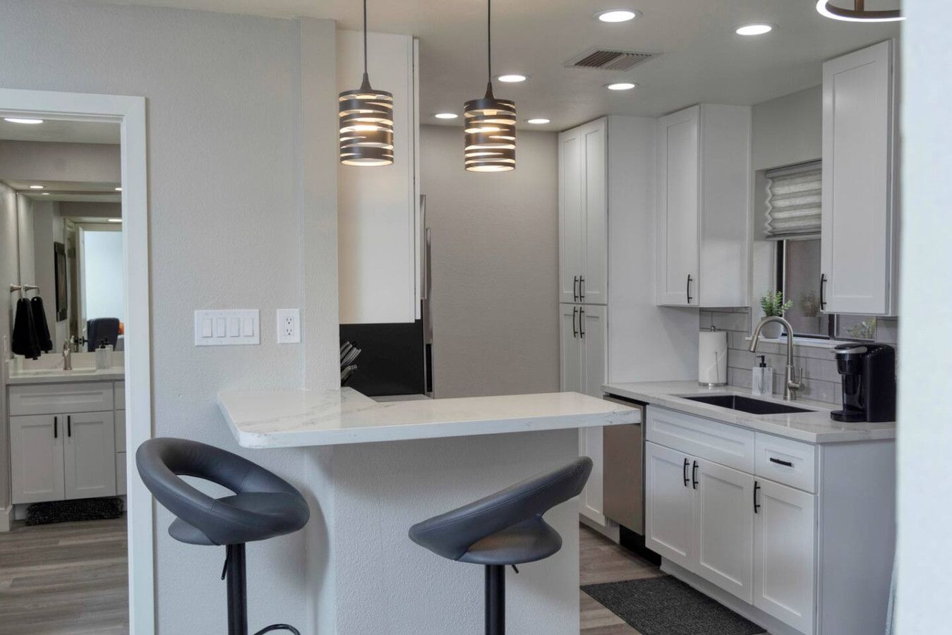 A modern kitchen with white cabinets, a bar area with stools, and pendant lighting.