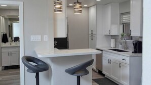 A modern kitchen with white cabinets, a bar area with stools, and pendant lighting.