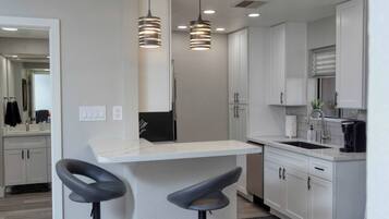 A modern kitchen with white cabinets, a bar area with stools, and pendant lighting.