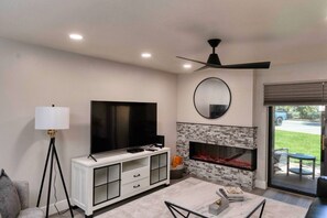 A living room with a flat-screen TV, a fireplace, a ceiling fan, and a dining area with a table and chairs.