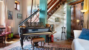 A grand piano in a room with a patterned rug, a bed with a blue pillow, and a staircase with wooden beams. - Apartment 'Il Flauto Magico' with Mountain View, Shared Garden and Wi-Fi (Serralunga d'Alba)