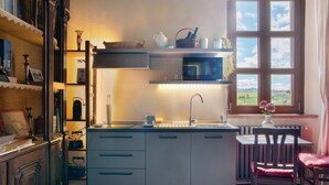 A kitchen with a microwave, sink, and wooden cabinets. There is a window with a view of the countryside. - Apartment 'Il Flauto Magico' with Mountain View, Shared Garden and Wi-Fi (Serralunga d'Alba)