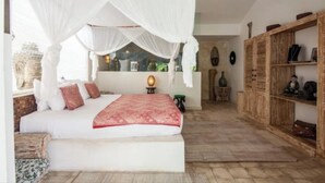 A bedroom with a canopy bed, a bedside table with a lamp, a wooden wardrobe, and a view of the city through the window. - VILLA BELLA SESEH (Cemagi)