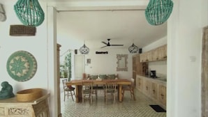 A dining area with a patterned floor, a wooden table, and chairs. There are hanging green lights above the table. - VILLA BELLA SESEH (Cemagi)