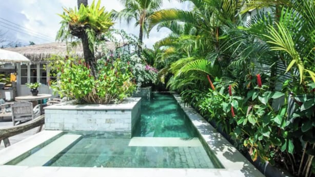 A pool area with a clear water feature, surrounded by lush tropical plants and a thatched roof structure. - VILLA BELLA SESEH (Cemagi)