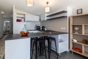 Una cucina moderna con isola centrale, sgabelli da bar, forno a microonde e macchina per il caffè.