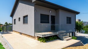 Une maison moderne à deux étages, dotée d’un balcon, d’un garage et d’une allée pavée.