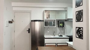 A compact kitchen with a refrigerator, microwave, and sink. There is a dining table with chairs. - Apto Allianz Metrô Barra Funda (Várzea da Barra Funda São Paulo)