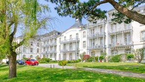 A multi-story hotel with balconies, a garden area, and parked cars. - Apartment 'Appartement Face Mer Et Piscine' with Sea View, Shared Pool and Wi-Fi (Le Croisic)