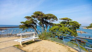 A coastal walkway with a wooden bench, metal railing, and trees overlooking the sea. - Apartment 'Appartement Face Mer Et Piscine' with Sea View, Shared Pool and Wi-Fi (Le Croisic)