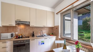 A modern kitchen with white cabinets, a built-in oven, a microwave, and a window with a view of greenery. - Garden on the Lake 1 in Vira Gambarogno, Gambarogno, Vira, Switzerland (Gambarogno, Vira)