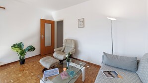 A living room with a glass coffee table, a beige armchair, a grey sofa, a potted plant, and a framed quote on the wall. - Garden on the Lake 1 in Vira Gambarogno, Gambarogno, Vira, Switzerland (Gambarogno, Vira)