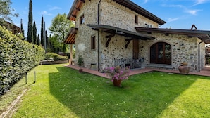Ein Steinhaus mit geneigtem Dach, einer überdachten Veranda und einem gepflegten Rasen.