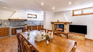 Eine geräumige Küche mit Esstisch, Holzschränken, einem Steinkamin und einem an der Wand montierten Fernseher.