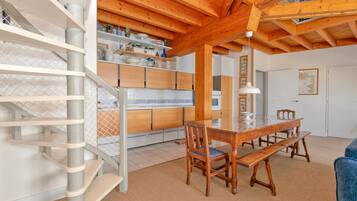 Une cuisine moderne avec des poutres en bois, une table à manger avec des bancs et un escalier doté d’une rampe.