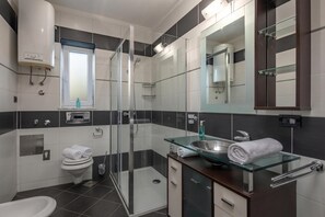 A modern bathroom with a glass shower enclosure, a glass sink, a toilet, and a mirror.