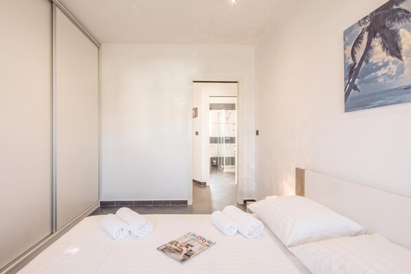 Een hotelkamer met een bed, twee opgerolde handdoeken, een tijdschrift en een schilderij van een palmboom.