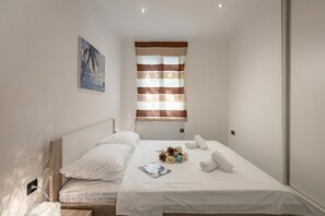 Ein Schlafzimmer mit einem Bett, Kissen, einem Nachttisch, einem Fenster mit Jalousien und einem Gemälde an der Wand.