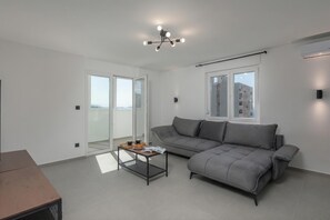 Un salón moderno con un sofá gris, un ventanal que da al exterior y una lámpara en el techo.